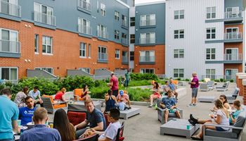 a group of people sitting and standing on a patio in front of an apartment building
